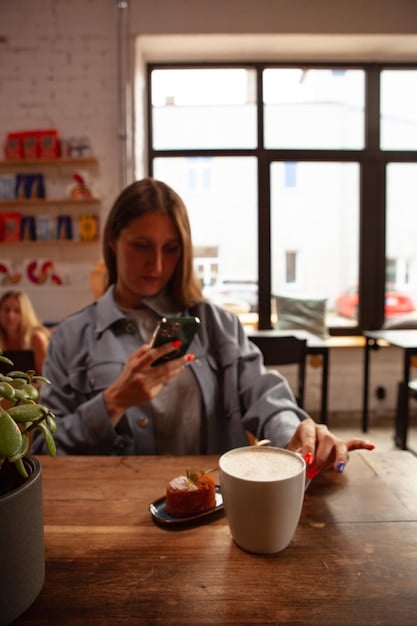 A person using a Pomodoro app on their smartphone while working at a coffee shop. The app displays a timer set to 25 minutes, and the person is taking notes in a notebook. The scene shows the technique being used in a real-world setting.