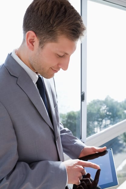 A close-up of a project manager using a time tracking app on a tablet, showing detailed reports and analytics of team members' task durations and overall project progress. The background is blurred, focusing on the tablet screen and user's hands.