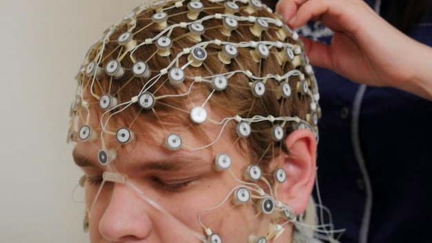 A close-up shot of EEG electrodes placed on a person's head, concentrating on the sophisticated technology and the data signals being received and processed in real-time. The background is minimalist and professional, emphasizing the focus on the biofeedback equipment and the subject's interaction with the technology for brain training.