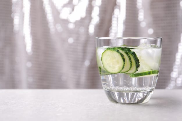 Clear glass filled with fresh water, with slices of lemon and cucumber floating inside, placed on a wooden surface, highlighting hydration and healthy living related to better focus.